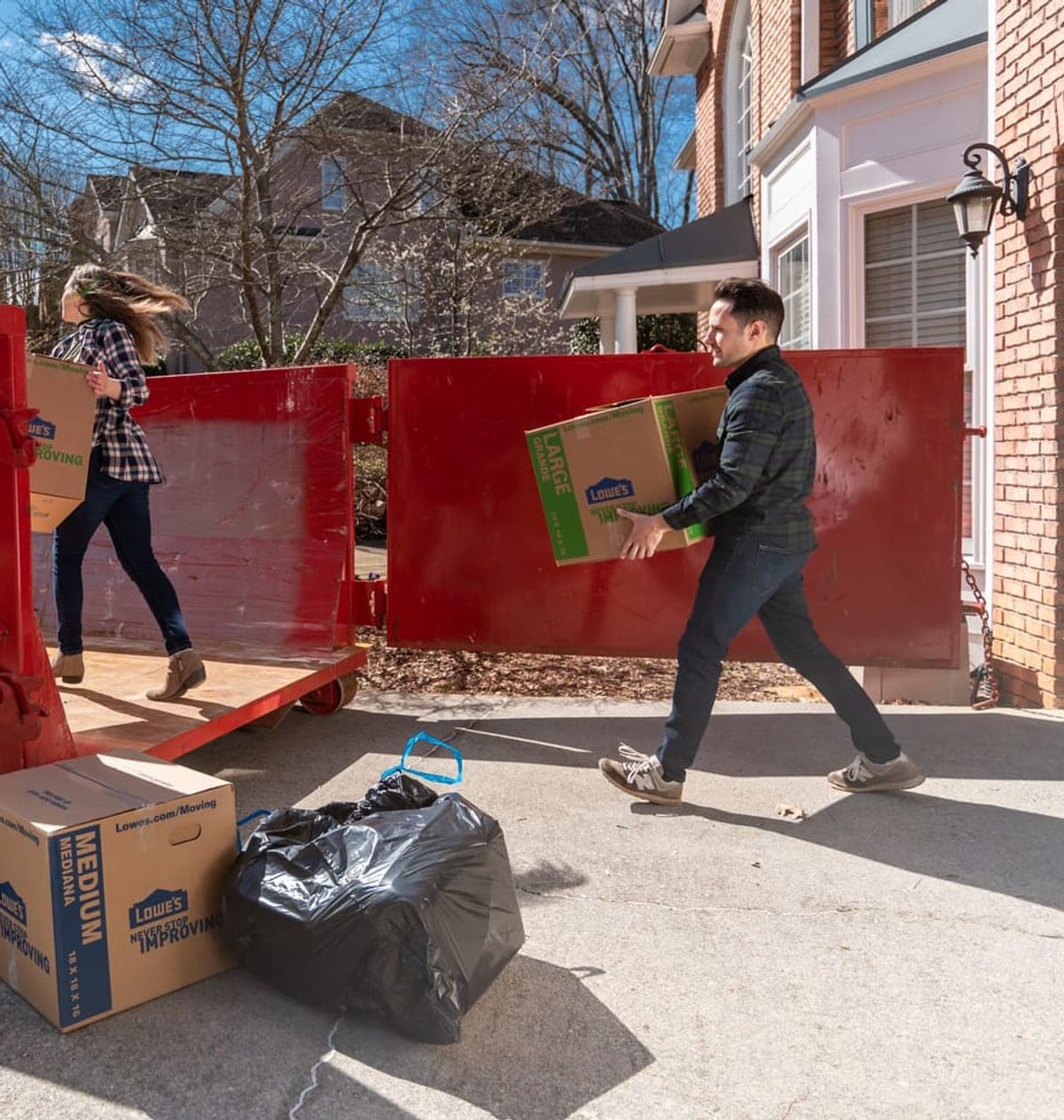 Homeowners loading moving boxes into a roll-off dumpster in their driveway