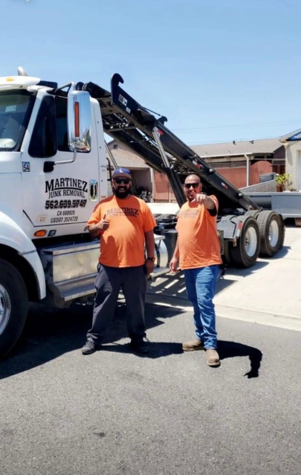 Mario Martinez, owner of Martinez Junk Removal (right), in front of a company roll-off dumpster truck.